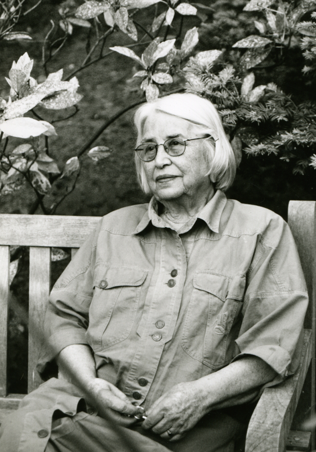 schwarzweißes Portrait von Annemarie Böll in hohem Alter auf einer Parkbank zwischen Magnolien