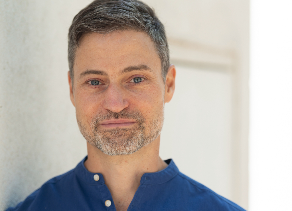 Portrait des Autors Meron Mendel in blauem Hemd vor hellem Hintergrund