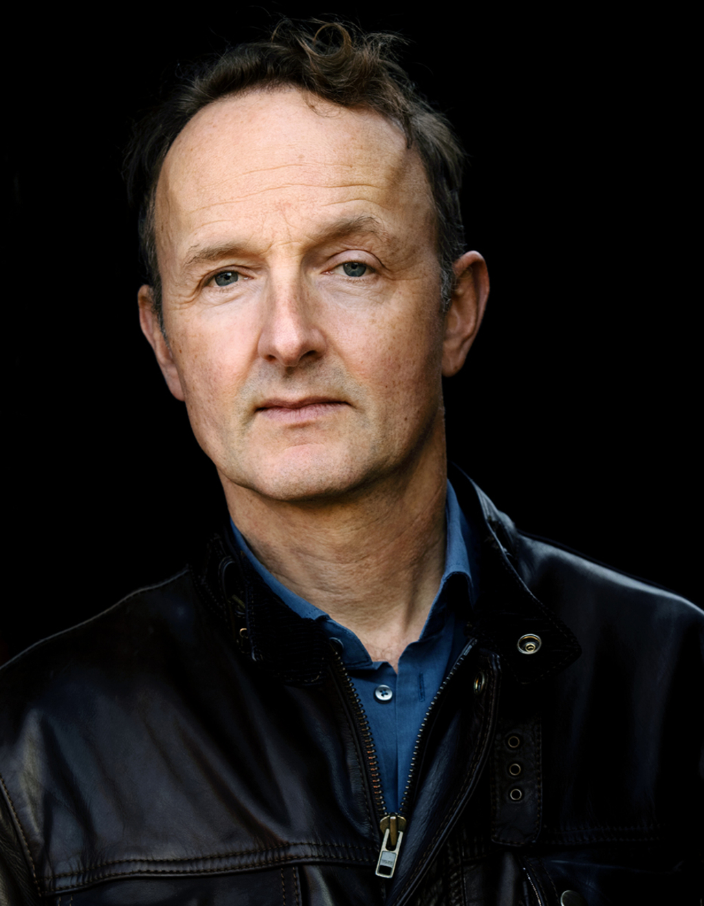 Porträt des Autos und Schauspielers Peter Jordan. Er steht mit schwarzer Lederjacke vor einem schwarzen Hintergrund. Sein Gesichtsausdruck ist ernst und eine Augenbraue angehoben.