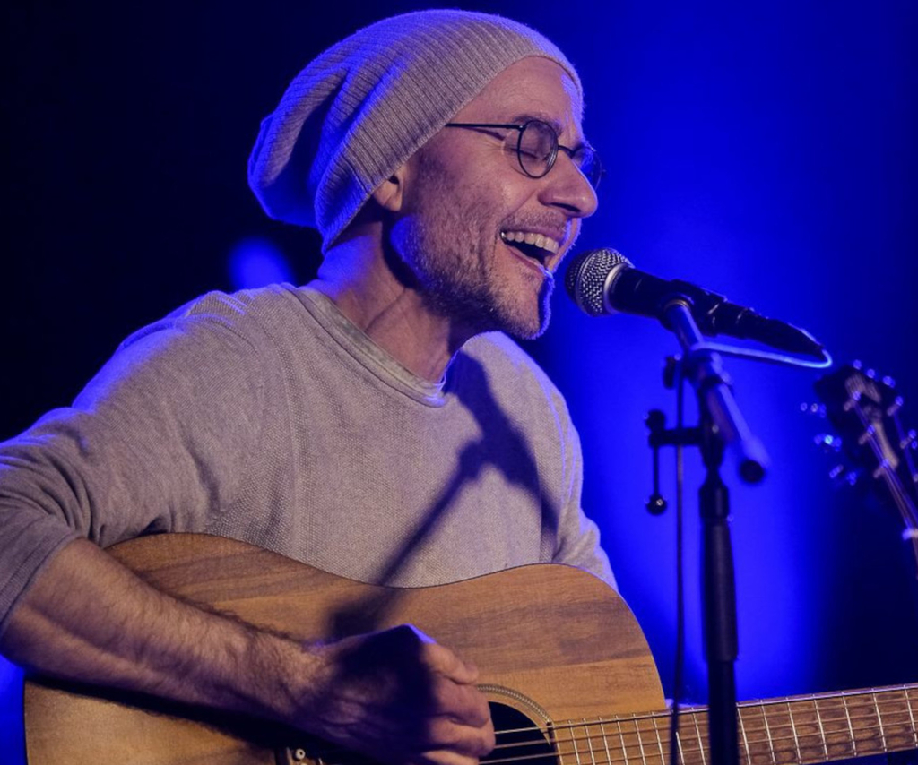 Portrait von Rudolf Könen, mit Gitarre und in ein Mikrofon singend