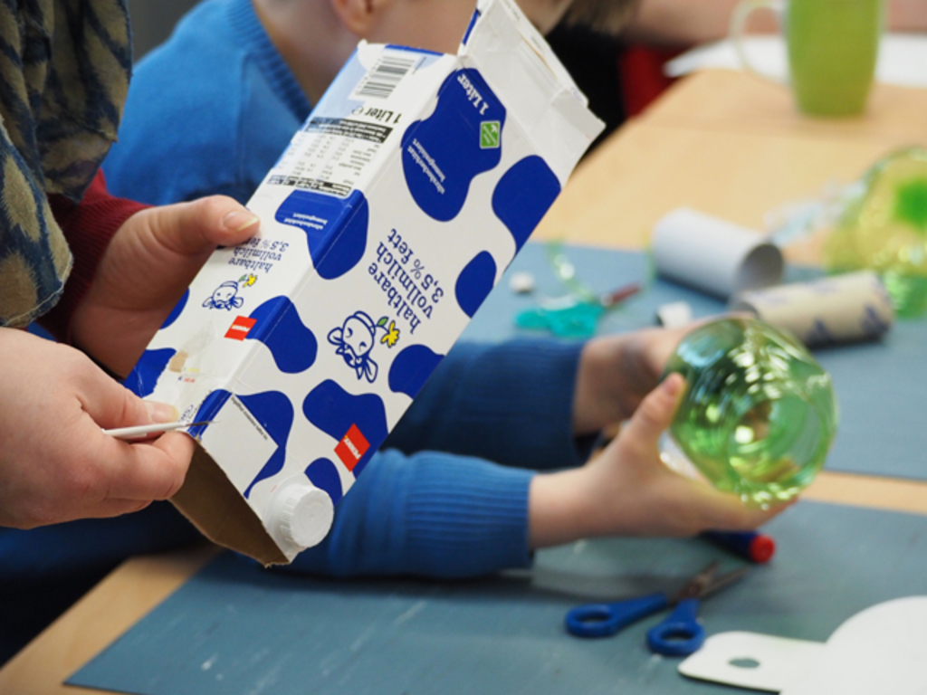 Kinder beim Upcycling - eine alte Milchtüte im Vordergrund