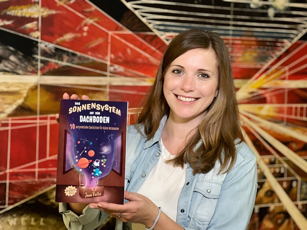Die Autorin Jana Ruster ist zusammen mit ihren Buch, das Sonnensystem auf dem Dachboden, abgebildet.