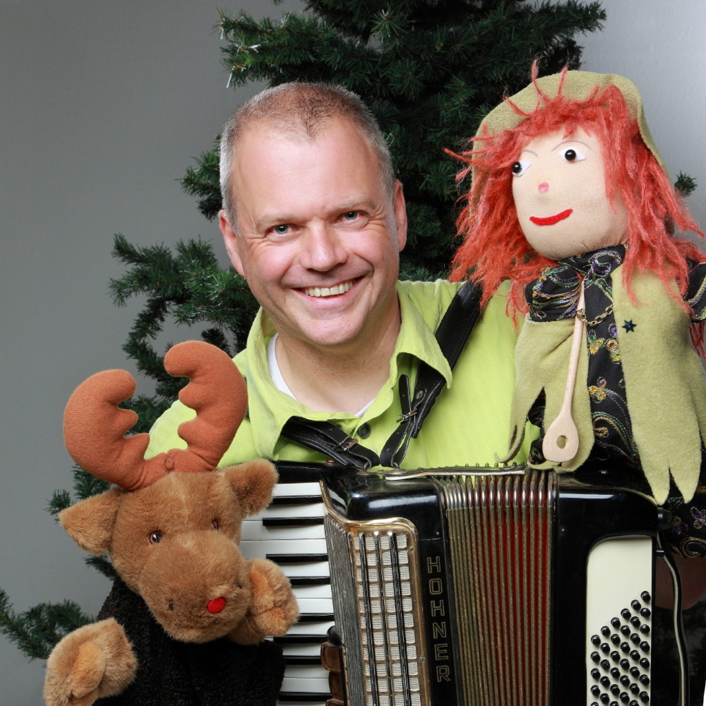 Anders Orth ist abgebildet mit einer Puppe, einem Akkordeon und einem Stofftiert-Elch