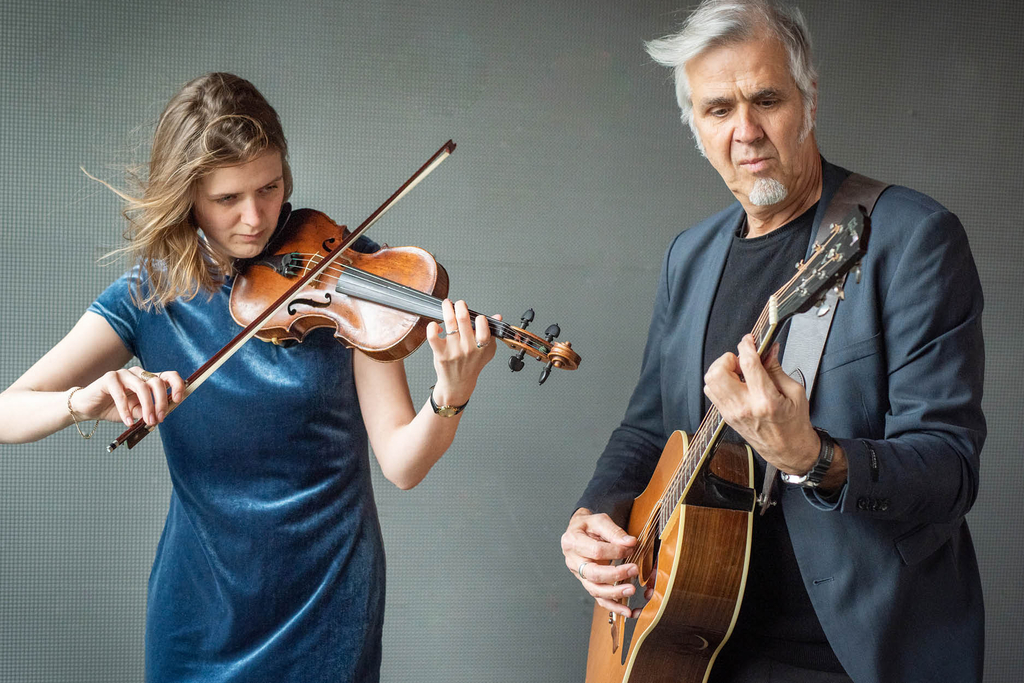 Ein Foto von Celiné und Thomas Wirtz, wie sie vor einer Studioleinwand ihre Instrumente spielen.