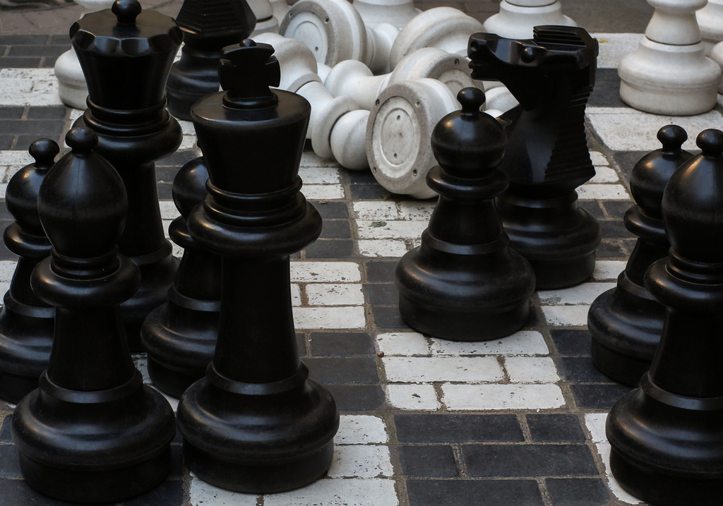 Figuren eines Riesenschach stehen auf abgenutzten Fliesen im Schachbrettmuster