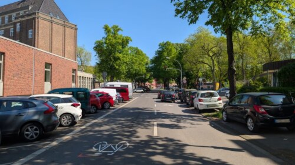 Foto der Mommsenstraße in Lindenthal. Zu sehen sind an der Seite geparkte Autos. In der Mitte sind großflächige Fahrradpiktogramme aufgebracht, eine sogenannte "Piktogrammkette"., Link auf Piktogrammketten für den Radverkehr