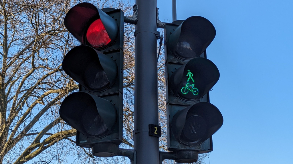 Foto einer Ampel mit grünem Lichtsignal für Fußgänger und Radfahrende und rotem Lichtsignal für den Autoverkehr