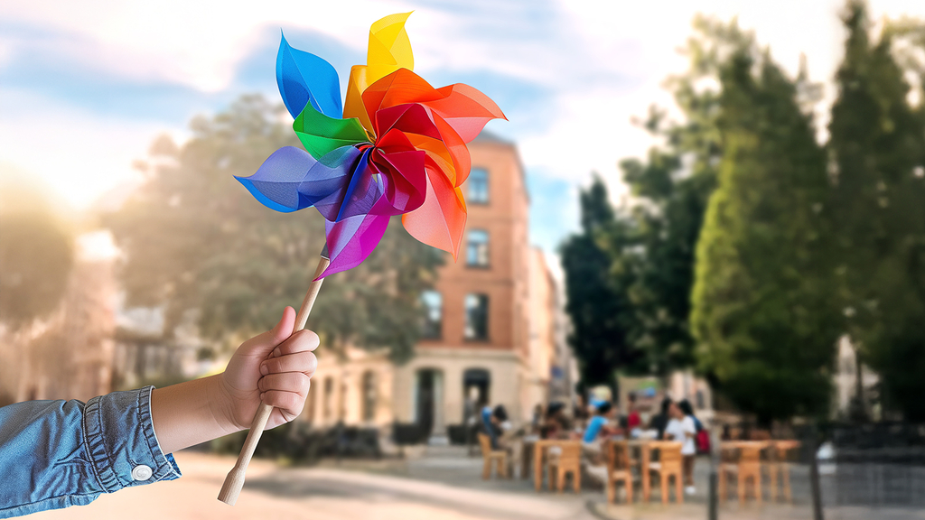 Windrädchen in Kinderhand. Im Hintergrund sieht man die Fassade eines Hauses mit Menschen auf Stühlen davor., Link auf Bürgerrat "Mobil im lebenswerten Quartier"