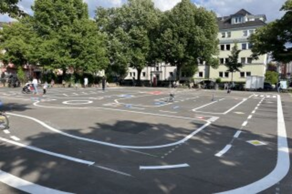 Verkehrsübungsplatz Auerbachplatz. Zu sehen sind markierte Flächen sowie Kinder, die die Fläche nutzen., Link auf Verkehrsübungsplätze in Köln