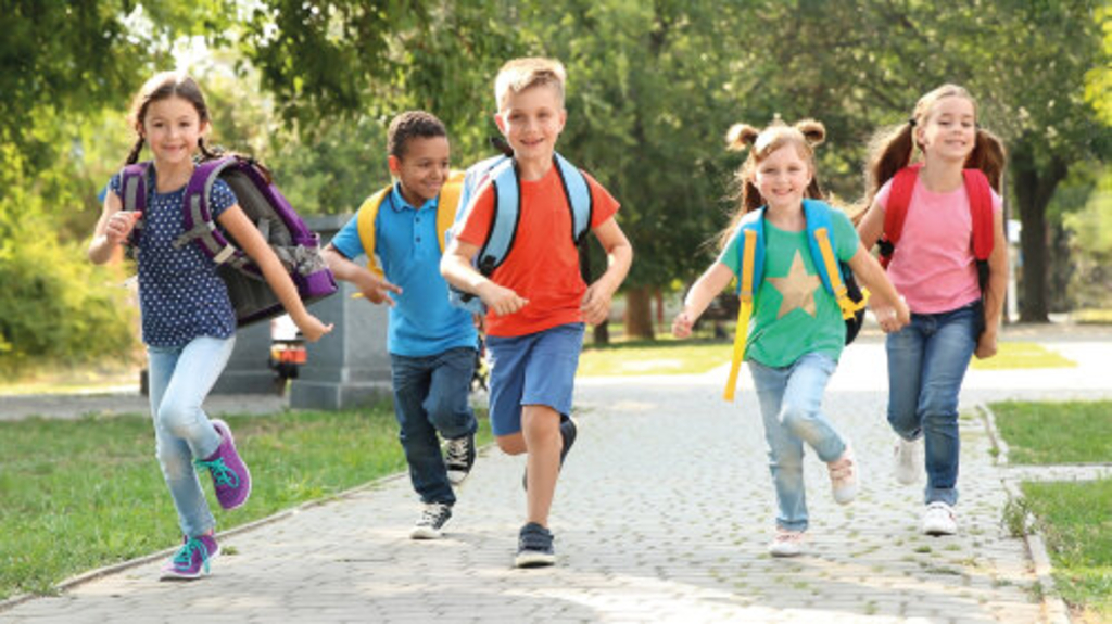 Fünf Kinder mit Schulranzen auf dem Rücken laufen durch einen Park Richtung Schule, Link auf Tipps zum Schulbeginn - Stadt Köln