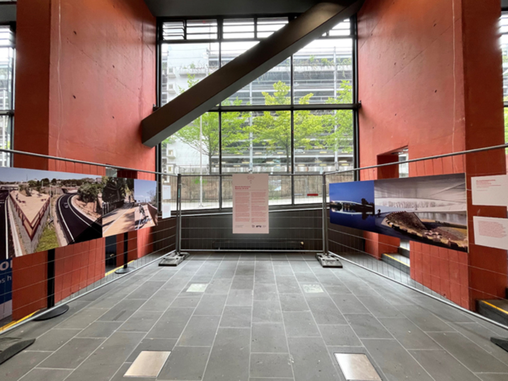 Ausstellung Bicycle Archtiectur Biennale. Zu sehen sind Fotografien mit Texttafeln mit Beispielen besonderer Fahrradarchitektur aus aller Welt. Sie sind auf Bauzäunen montiert.