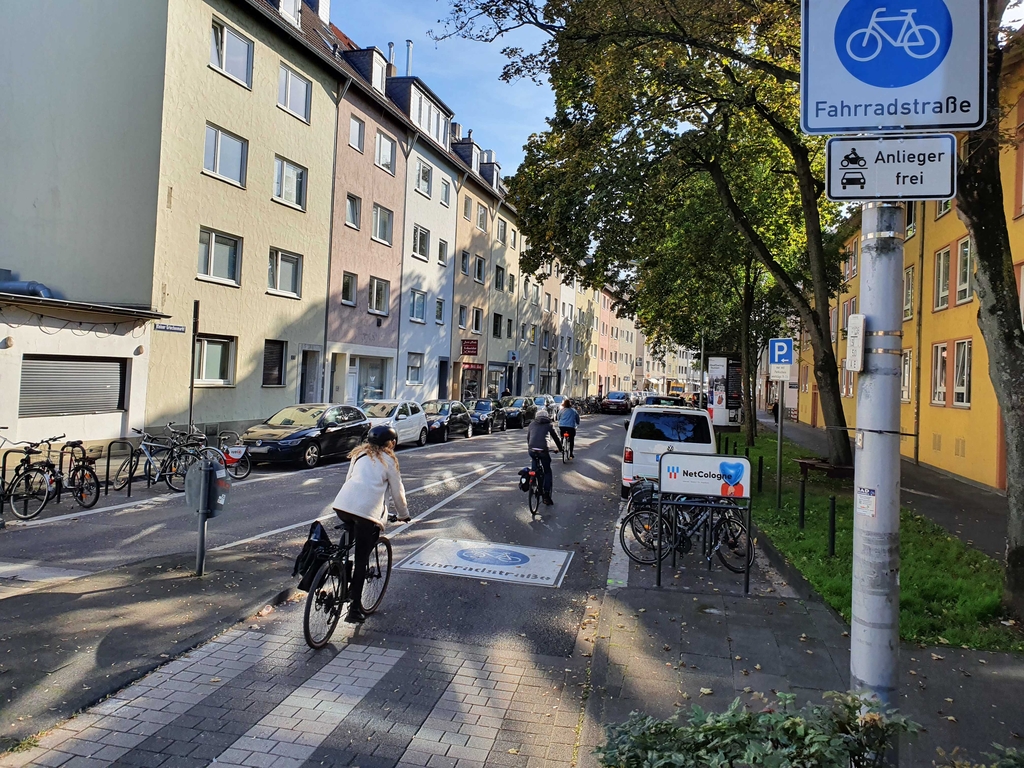 Drei Radfahrende, die auf der neu eingerichteten Fahrradstraße Kleiner Griechenmarkt unterwegs sind. Zu sehen ist ein großes Piktogramm "Fahrradstraße" auf der Fahrbahn.