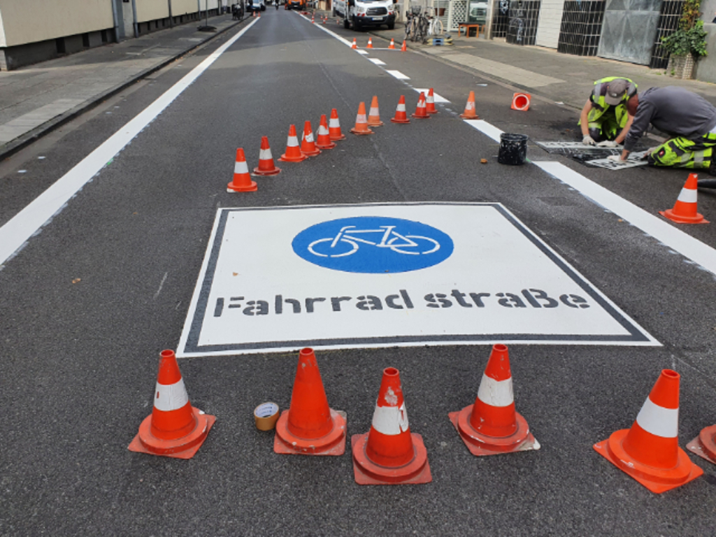 Auf der Straße Mauritiuswall wird der Hinweis Fahrradstraße markiert. Noch ist der Bereich abgesperrt durch Leitkegel.