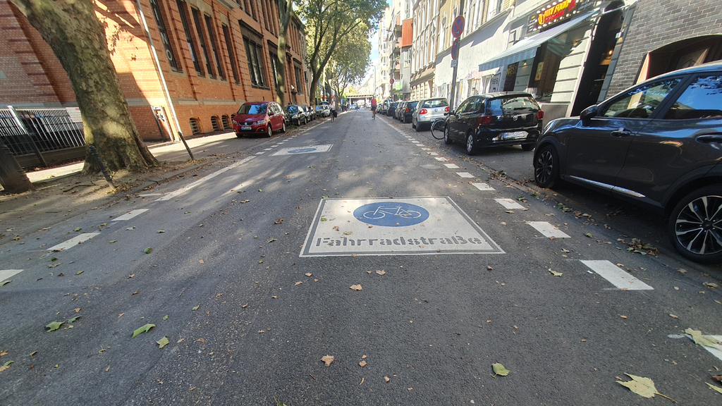 Quadratisches Fahrradstraßenpiktogramm mit einem blauen, runden Fahrrad-Symbol und der Aufschrift Fahrradstraße und ein Sicherheitstrennstreifen auf der Maybachstraße