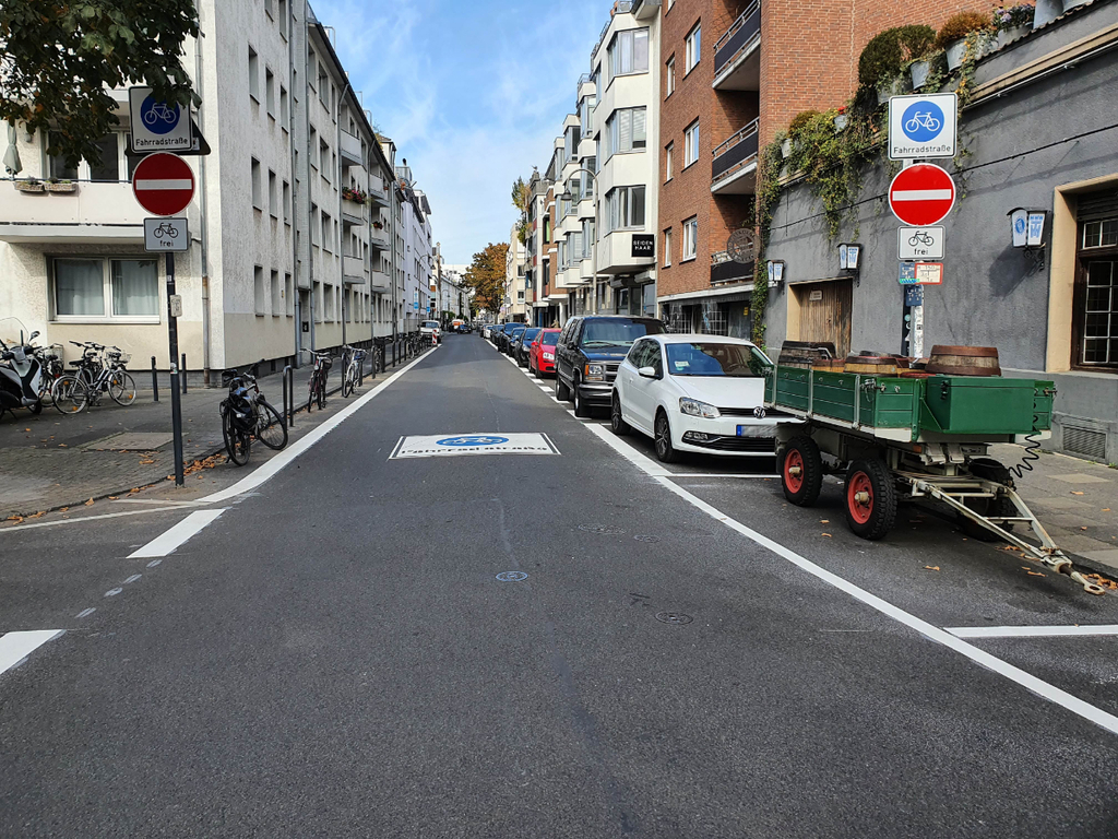 Neu eingerichtete Fahrradstraße Mauritiuswall. Auf der Fahrbahn ist ein großes Fahrradstraßenpiktogramm zu sehen. Die Autos parken rechts auf einem Parkstreifen. Die Gehwege sind freigeräumt.