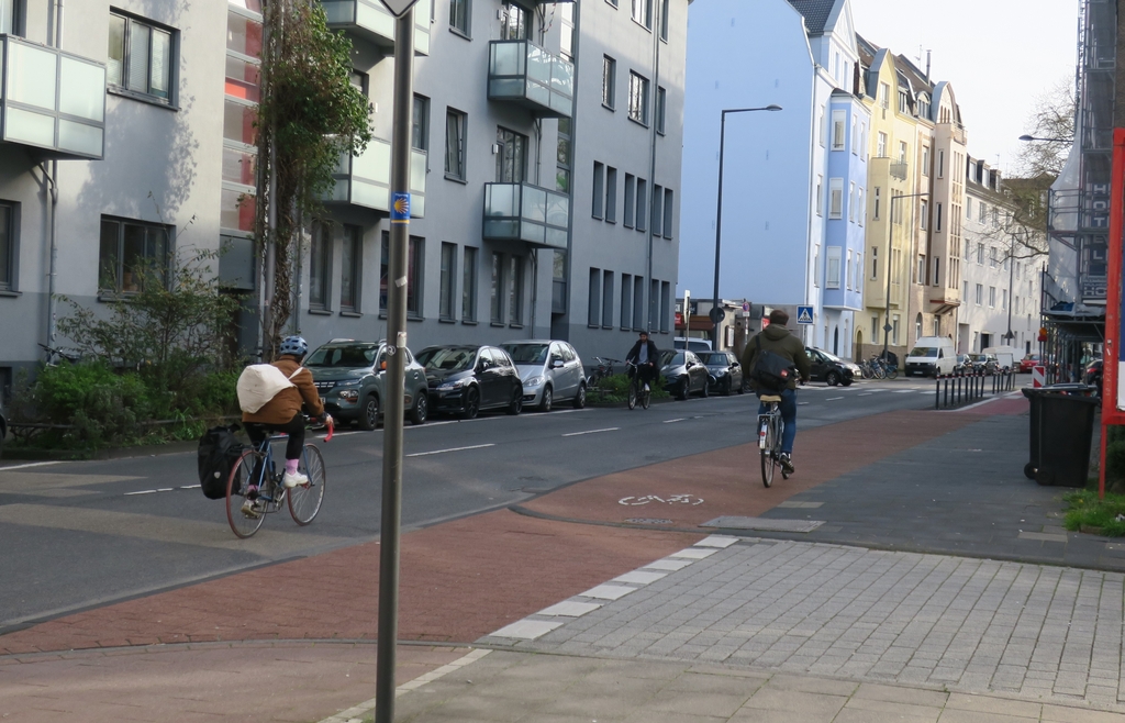 Zwei Radfahrende fahren auf der Fahrbahn, ein Radfahrender nutzt den rot markierten Radweg