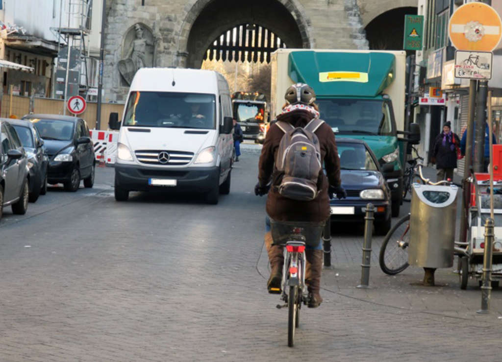 Radfahrerin fährt in eine für Radfahrer freigegebene Einbahnstraße ein; ein weißer Transporter kommt ihr entgegen.