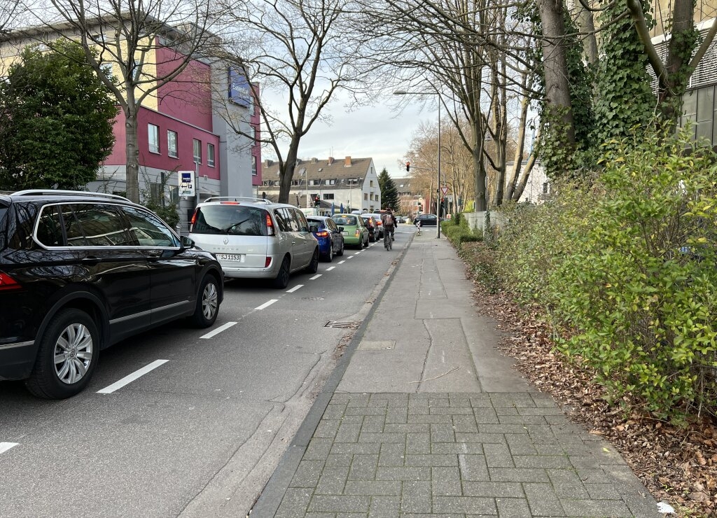 Radfahrender auf neuem Fahrradschutzstreifen an wartenden Autos an der Ampel vorbeifahrend Richtung Aachener Straße