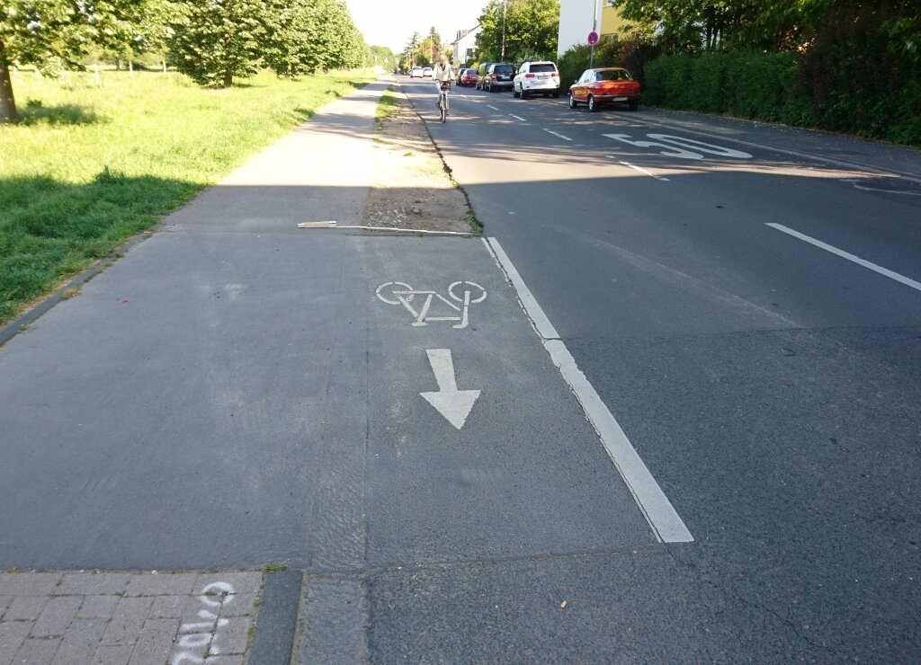 kurze Ausschleusung vom gemeinsamen Gehweg und Radweg mit Fahrradpiktogramm und Geradeauspfeil, Radfahrender fährt auf der Straße neben dem gemeinsamen Gehweg und Radweg