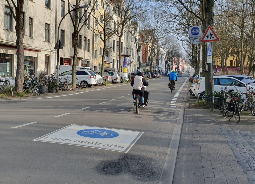 Zwei Radfahrende auf der Fahrradstraße Weyertal mit neuem Sicherheitstrennstreifen und neuem Fahrradstraßenpiktogramm