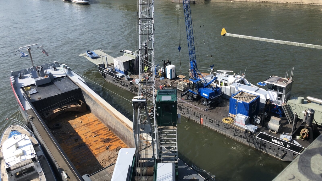 Arbeiten zur Verschließung der Bohrlöcher. Zu sehen sind zwei Schiffe mit Baggern auf dem Rhein.