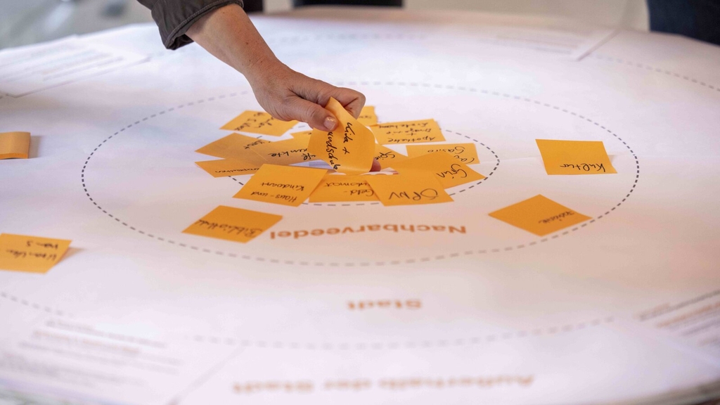 Foto von einer Hand, die einen Notizzettel an einer Planwand festmacht. Das Foto entstand in einer Veranstaltung für den nachhaltigen Mobilitätsplan.