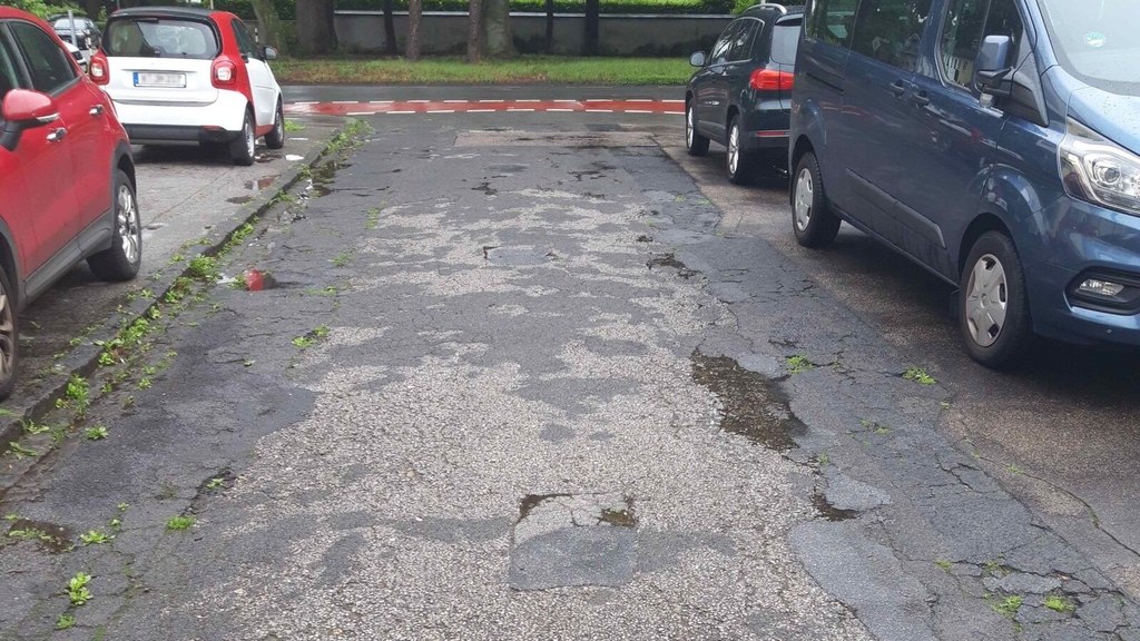 Blick in die Straße Falkenweg. Die Straßendecke zeigt starke Beschädigungen auf.