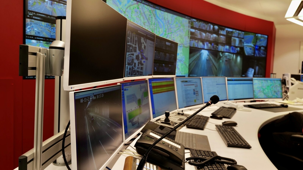 Foto der Verkehrs- und Tunnelleitzentrale. Zu sehen sind die Monitore mit den Verkehrsbeobachtungskameras, eine digitale Übersichtskarte mit den Ampelanlagen und eine Vielzahl weiterer Monitore.