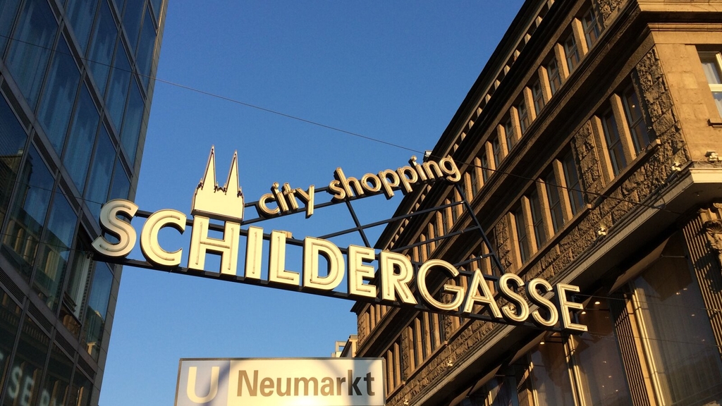 Beginn der Einkaufsstraße Schildergasse. Über die Straße ist ein Schild gespannt mit city shopping Schildergasse., Link auf Bessere Wege zu den Einkaufsstraßen