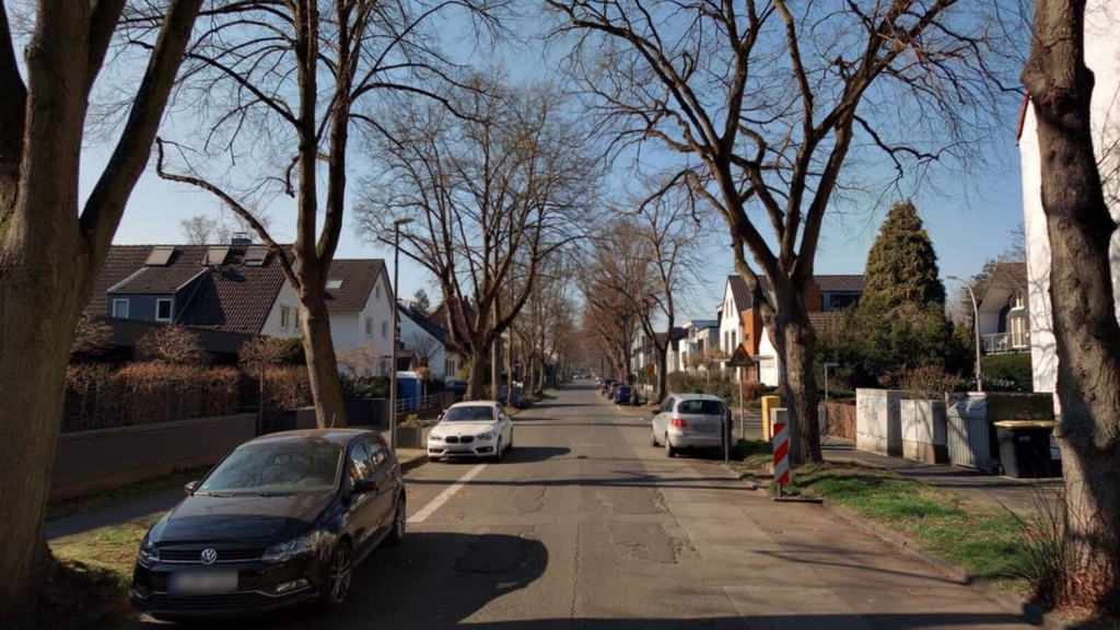 Foto des Auenwegs mit beschädigter Straßendecke. An der Seite stehen Fahrzeuge.