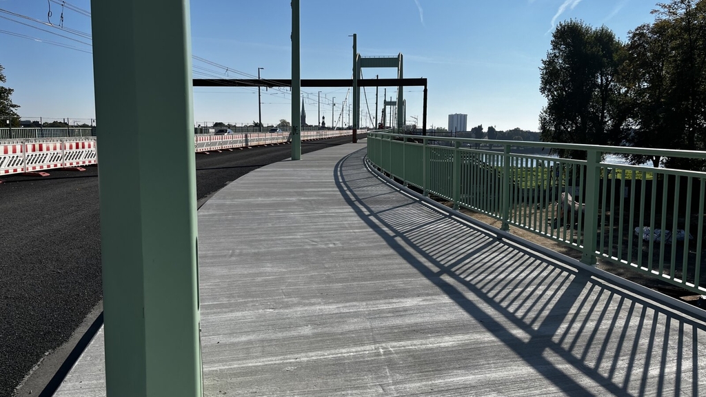 Zu sehen ist der Geh- und Radweg der Mülheimer Brücke im Bereich der Deichbrücke. Das Geländer wirft einen Schatten.