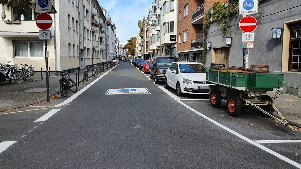 Foto der neu eingerichteten Fahrradstraße Mauritiuswall. Auf der Fahrbahn zu sehen ein großes Fahrradstraßenpiktogramm. Die Autos parken rechts auf einem Parkstreifen. Die Gehwege sind freigeräumt.