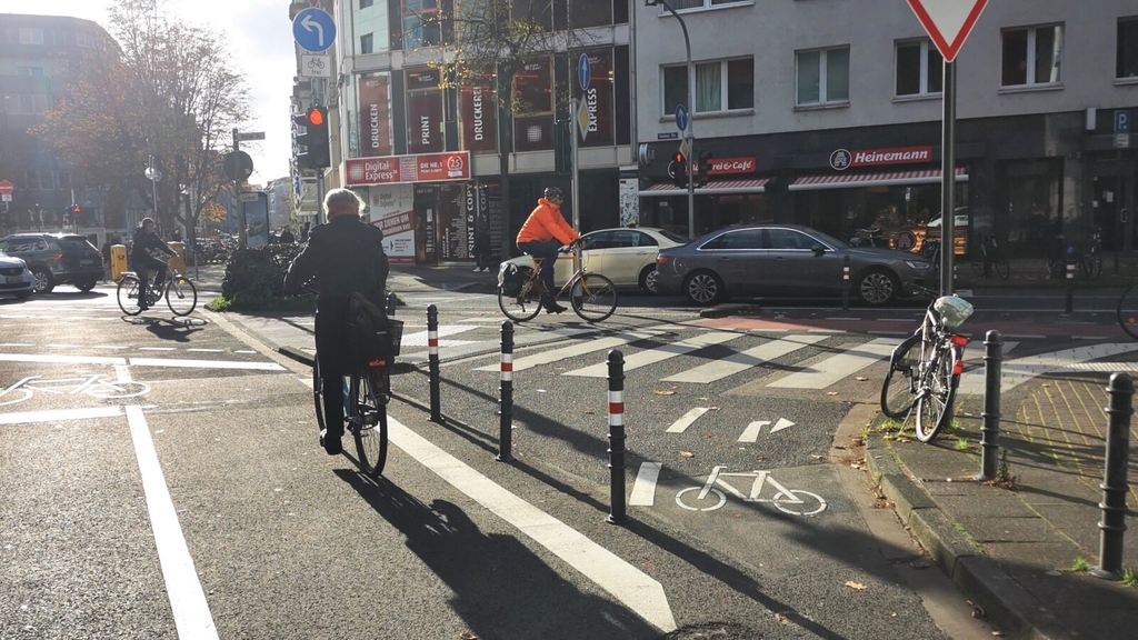 Zu sehen sind Radfahrende an der Kreuzung Venloer Straße/Kamekestraße. Die Abbiegespur in die Kamekestraße wurde für Autofahrende mit Pollern gesperrt.