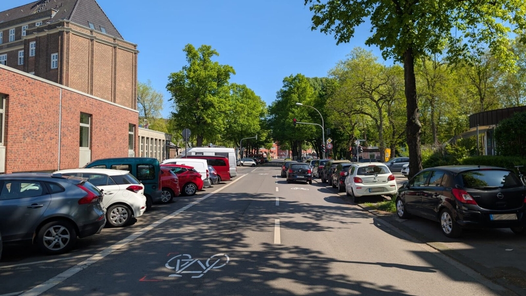 Foto der Mommsenstraße in Lindenthal. Zu sehen sind an der Seite geparkte Autos. In der Mitte sind großflächige Fahrradpiktogramme aufgebracht, eine sogenannte "Piktogrammkette".