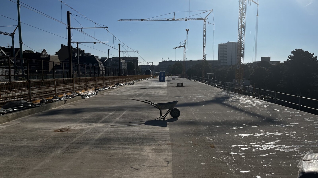 Zu sehen ist eine breite Asphaltfläche im Bereich der rechtsrheinischen Rampe der Mülheimer Brücke. In der Mitte steht eine Schubkarre.