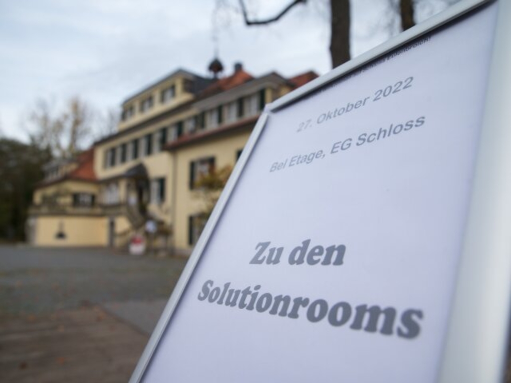 Foto eines Kundenstoppers mit dem Schloss Eulenbroich in Rösrath im Hintergrund. Auf dem Schild steht: 27. Oktober 2022, Bel Etage, EG Schloss, Zu den Solutionrooms