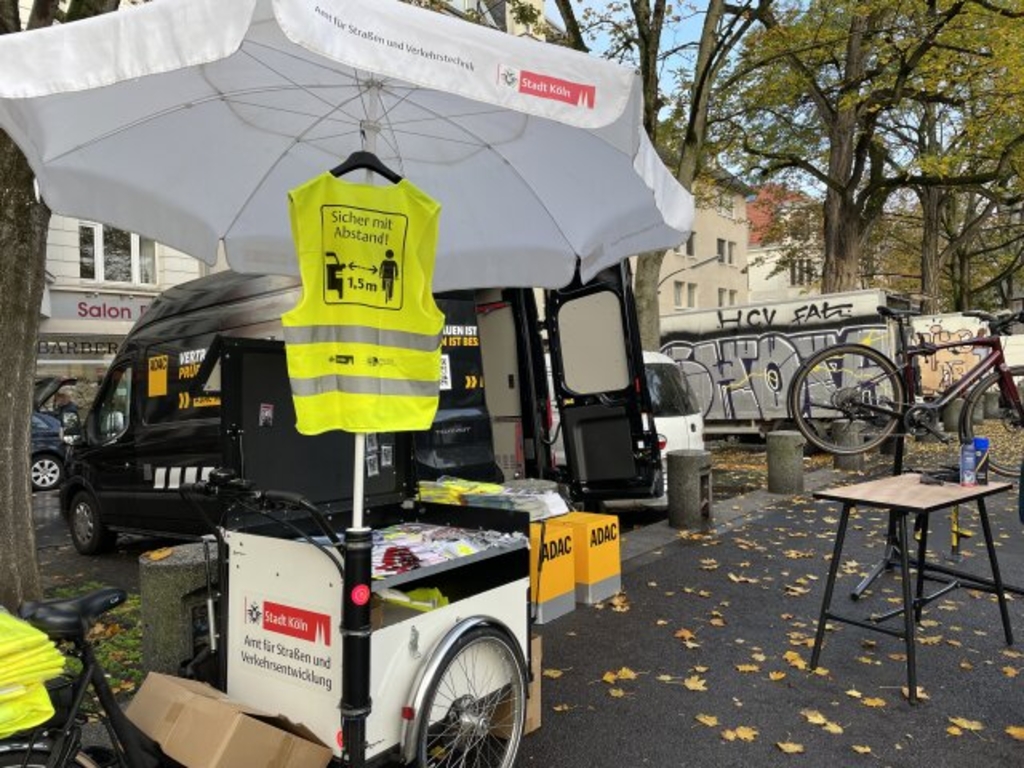 Stand des Fahrradbeauftragten auf dem Wilhelmplatz. Zu sehen ist ein Fahrradanhänger auf dem Infomaterial liegt. An einem weißen Sonnenschirm hängt eine Sicherheitswarnweste.