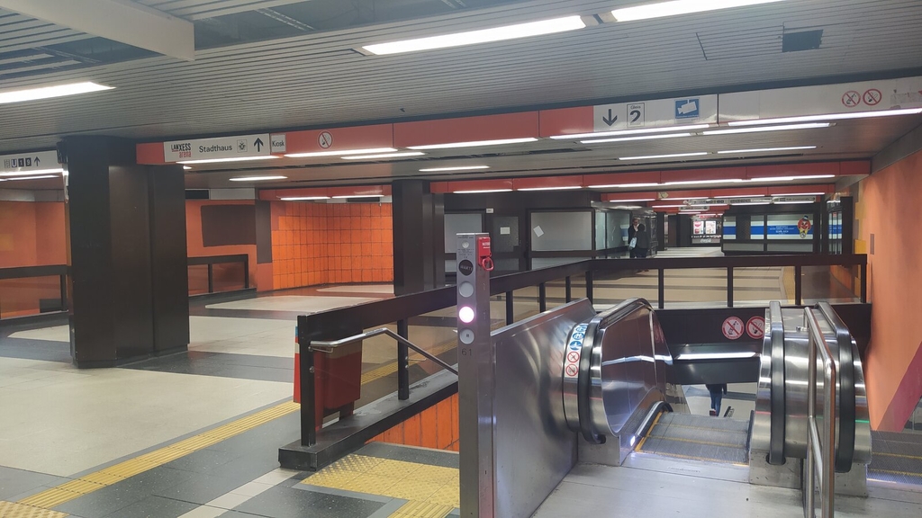 Zu sehen ist die Zwischenebene der Haltestelle Bahnhof Messe/Deutz. Im Vordergrund sind die Rolltreppen, welche zur Gleisebene der Stadtbahn führen. Im Hintergrund ist ein langer Flur., Link auf Sanierung der Stadtbahnhaltestelle Bahnhof Deutz/Messe