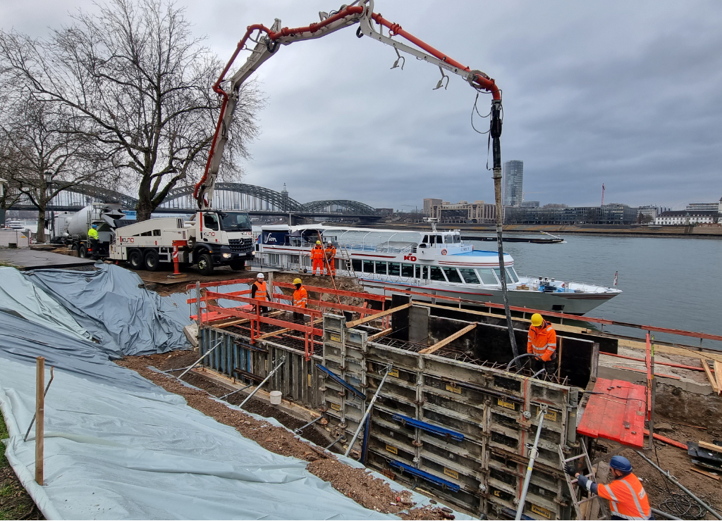 Das Foto zeigt die Betonpumpe mit dem dahinter stehenden Fahrmischer (Betonmischer), die am ersten Fundamentblock der Kragplatte arbeiten.