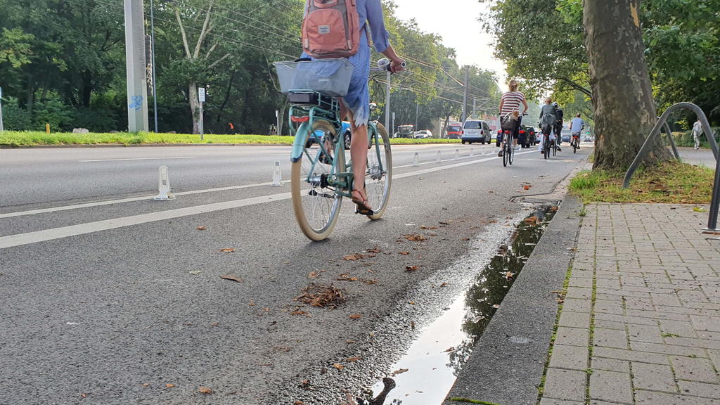 Radfahrende fahren über den mit sogenannten Sichtzeichen baulich getrennten neuen Radfahrstreifen auf der Aachener Straße in Höhe des Aachener Weihers
