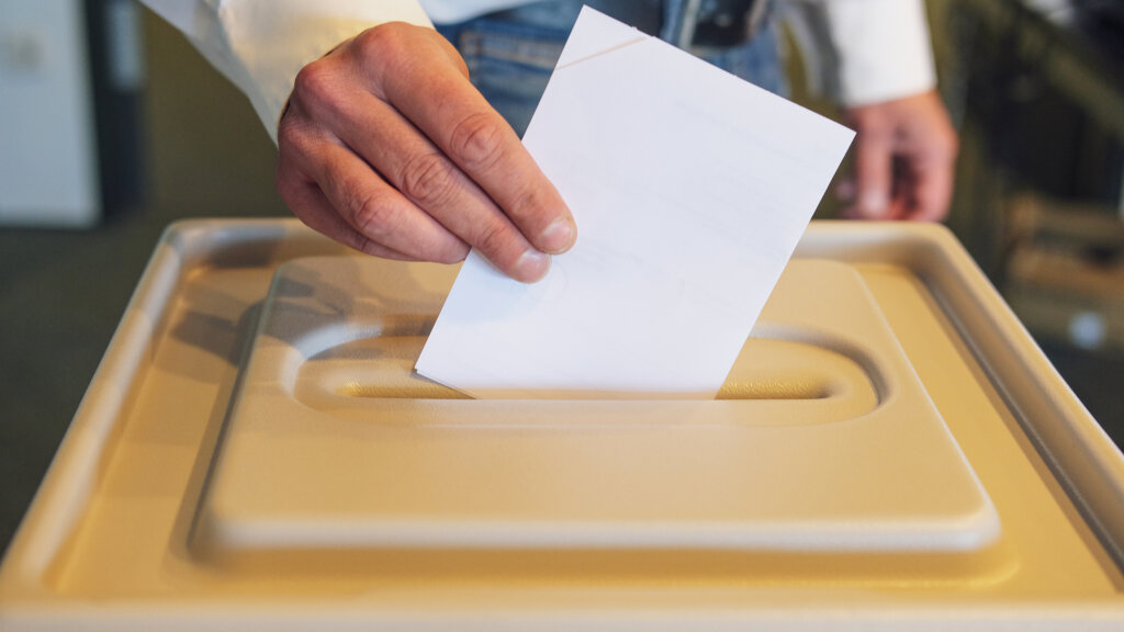 Mann wirft Stimmzettel in Wahlurne, Link auf Im Wahlraum wählen - Stadt Köln