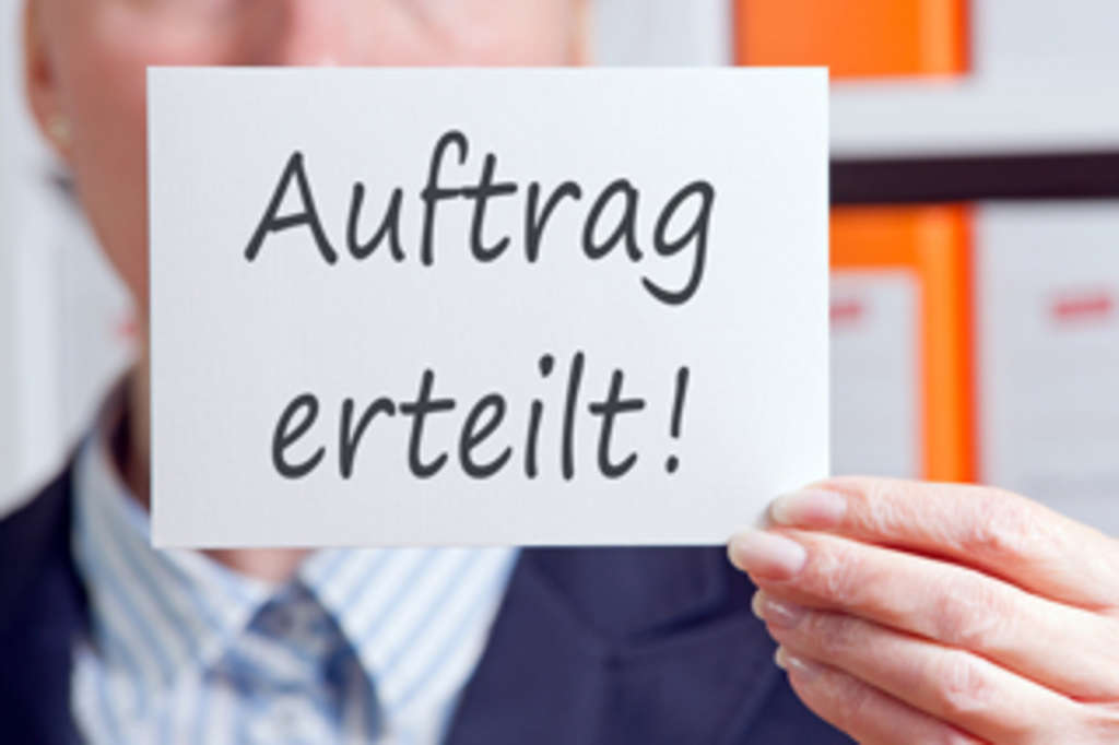 Man in Anzug hält Schild hoch, auf dem steht "Auftrag erteilt"