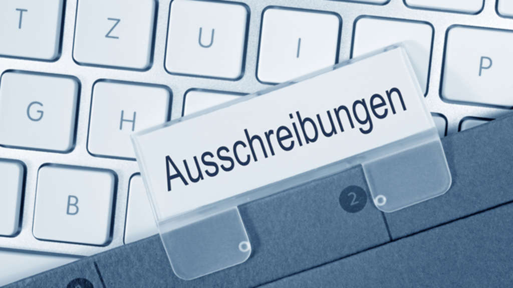 Im Hintergrund eine Tastatur, auf ihr liegt eine Mappe mit einem Schild, auf dem "Ausschreibungen" steht.