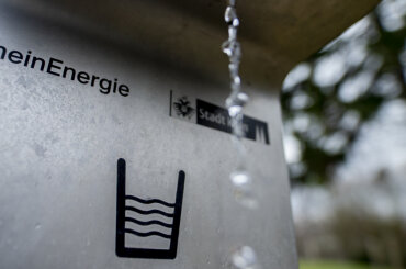 Nahaufnahme eines Trinkwasserbrunnens, der Wasserstrahl ist vor den Logos der RheinEnergie und der Stadt Köln sowie einer Wasserglas-Grafik zu sehen., © Thilo Schmülgen