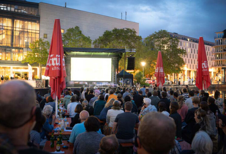 Menschenmenge mit Kopfhörern blicken auf eine Leinwand auf dem Platz  vorm Cinédom im Mediapark., © Simon Rupieper