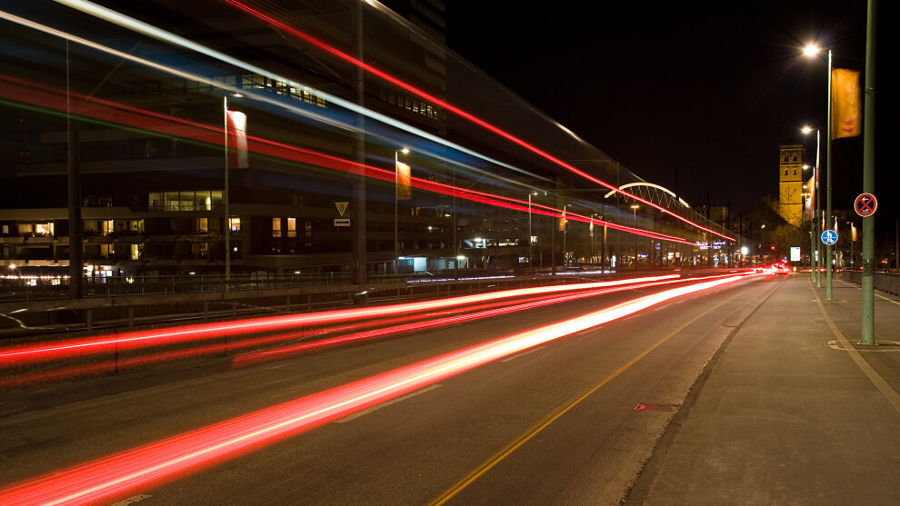 Straße bei Nacht - Die roten Rücklichter der Autos ziehen sich farblich durch das Bild.