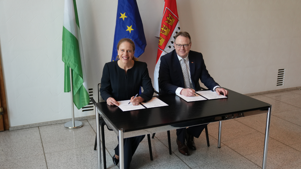 Oberbürgermeister Burmester und Bürgermeisterin Schouten sitzen an einem Tisch und unterzeichnen eine Vereinbarung zur Kooperation.