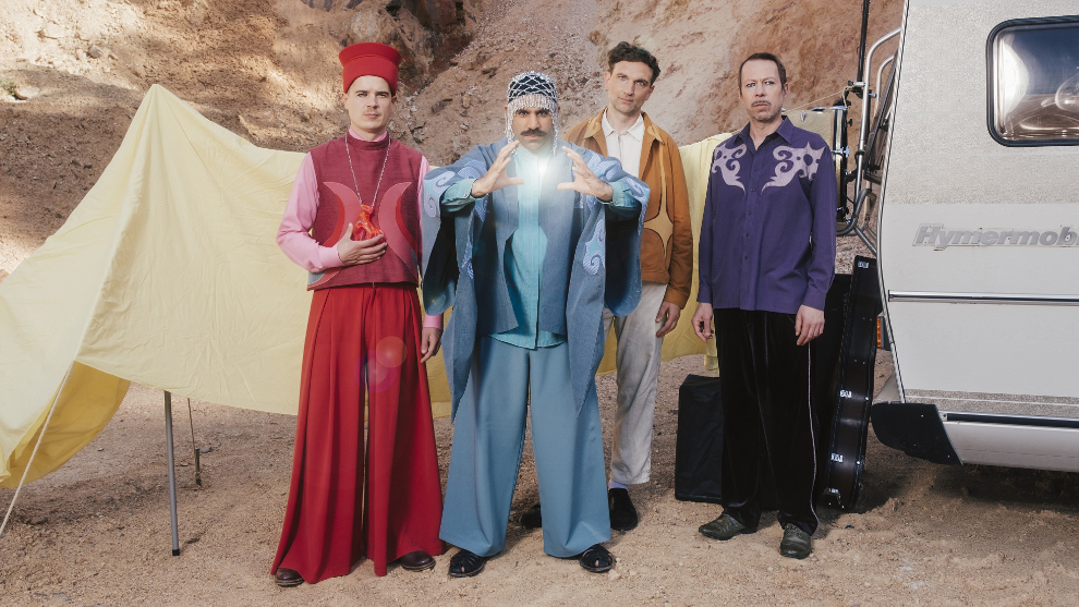 Foto von der Band "Keshavara". Die vier Mitglieder tragen bunte Klamotte und stehen in einer Wüstenlandschaft.