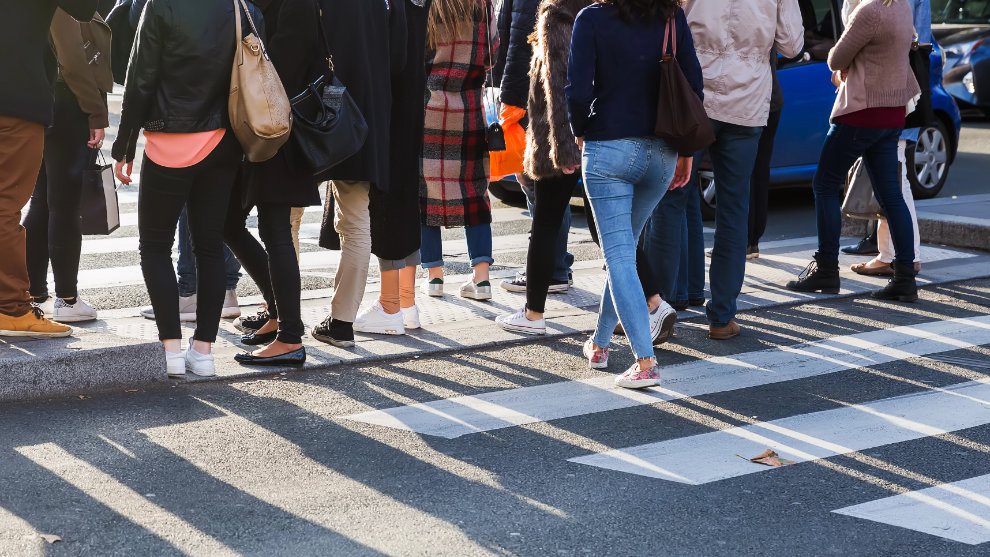 Menschen überqueren eine Straße über einen Zebrastreifen. Am oberen Rand ist das Foto so geschnitten, dass man keine Köpfe sieht.