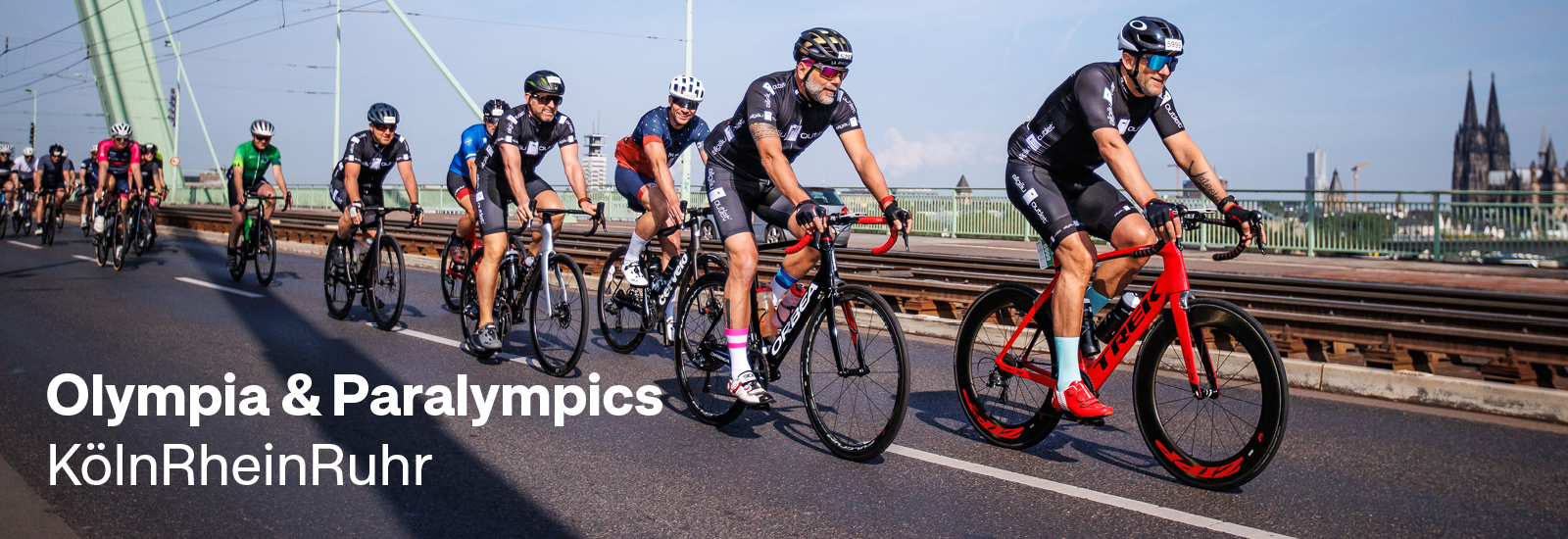 Mehrere Fahrradfahrer während eines Rennens auf der Rheinbrücke. Im Hintergrund sieht man den Kölner Dom.
